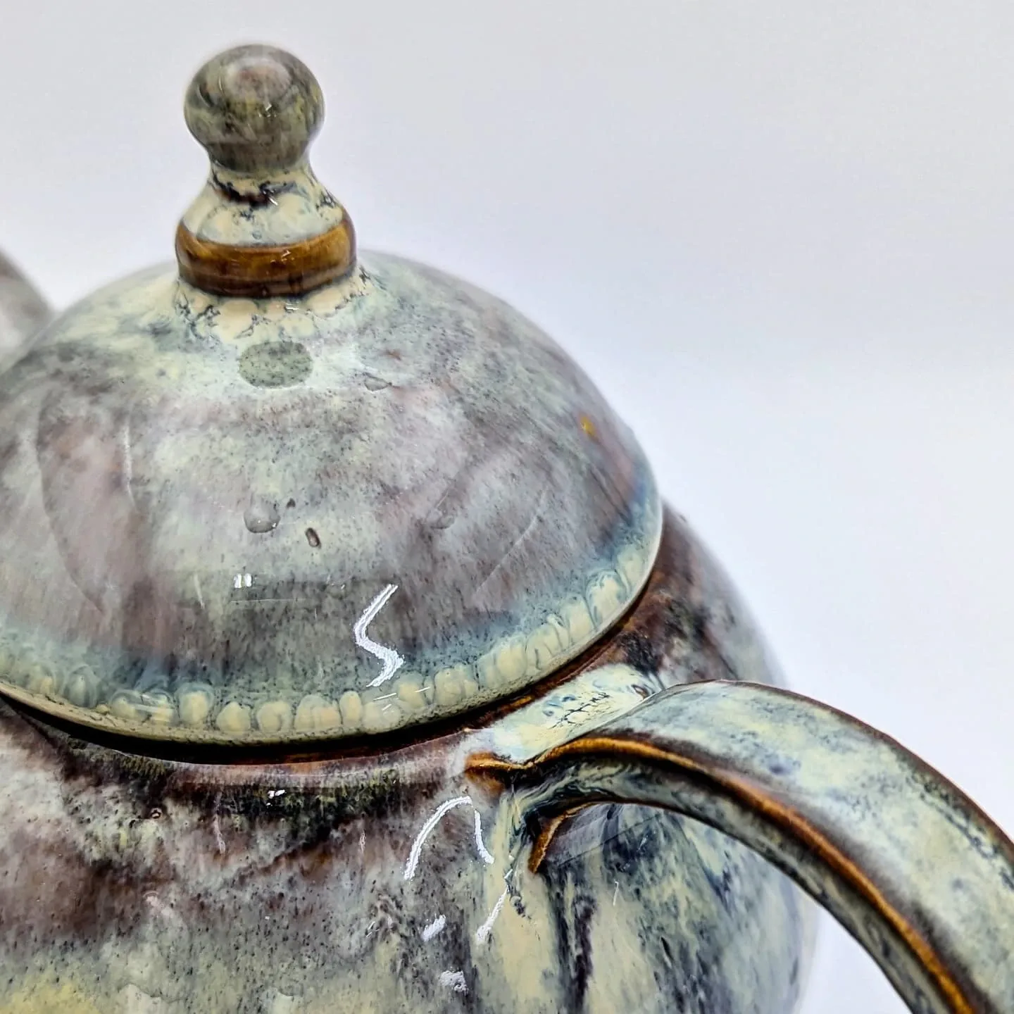 Close-up detail of a marbled grey and olive glaze on a teapot lid